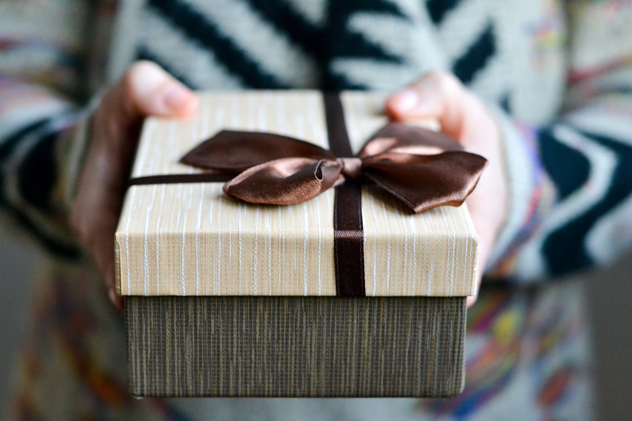 gallery-1 Stylish gift box with brown ribbon held in hands, perfect for holidays and celebrations.