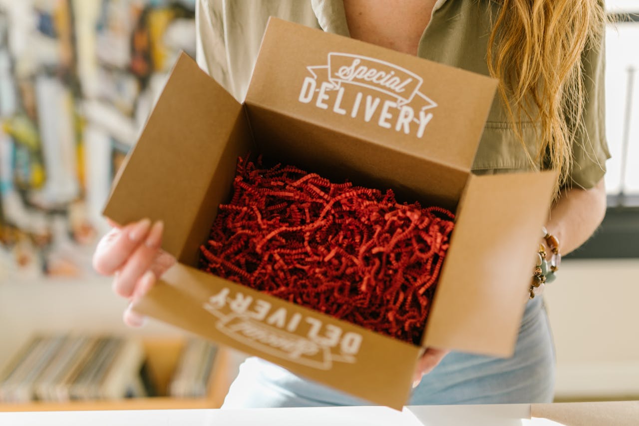 our-services-3 Person opening a special delivery box filled with red crinkle paper for secure packaging.