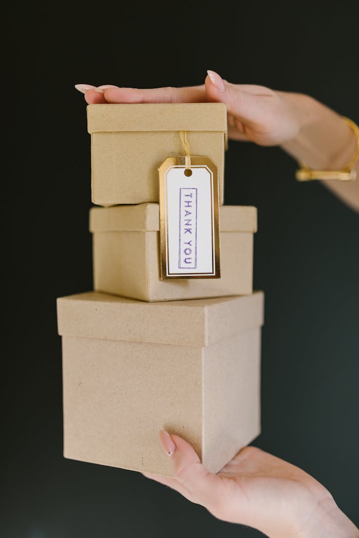 our-services-2 Three kraft gift boxes stacked with a 'Thank You' tag held by a woman's hands.