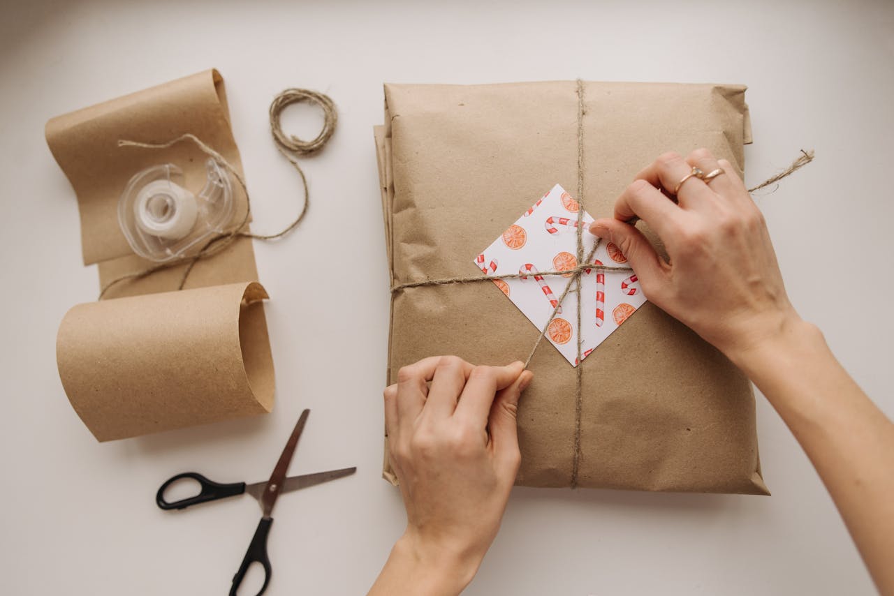 Hands tying a brown paper wrapped package with string, showcasing DIY gift wrapping.