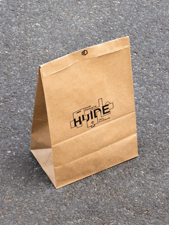 A standing kraft paper bag with custom print on a textured asphalt surface under sunlight.